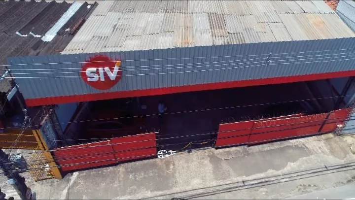 Vista aérea do galpão da SIV, com o selo vermelho da marca no letreiro e o pátio coberto de inspeção